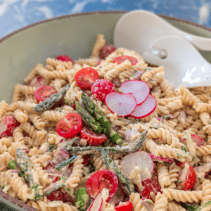 Delicious creamy pasta salad featuring fresh asparagus, cherry tomatoes, radishes, and mixed vegetab.
