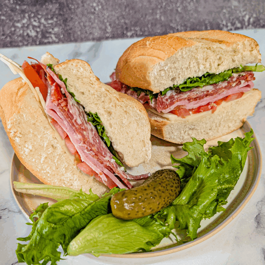 assorted sub sandwich cut open on plate with pickle