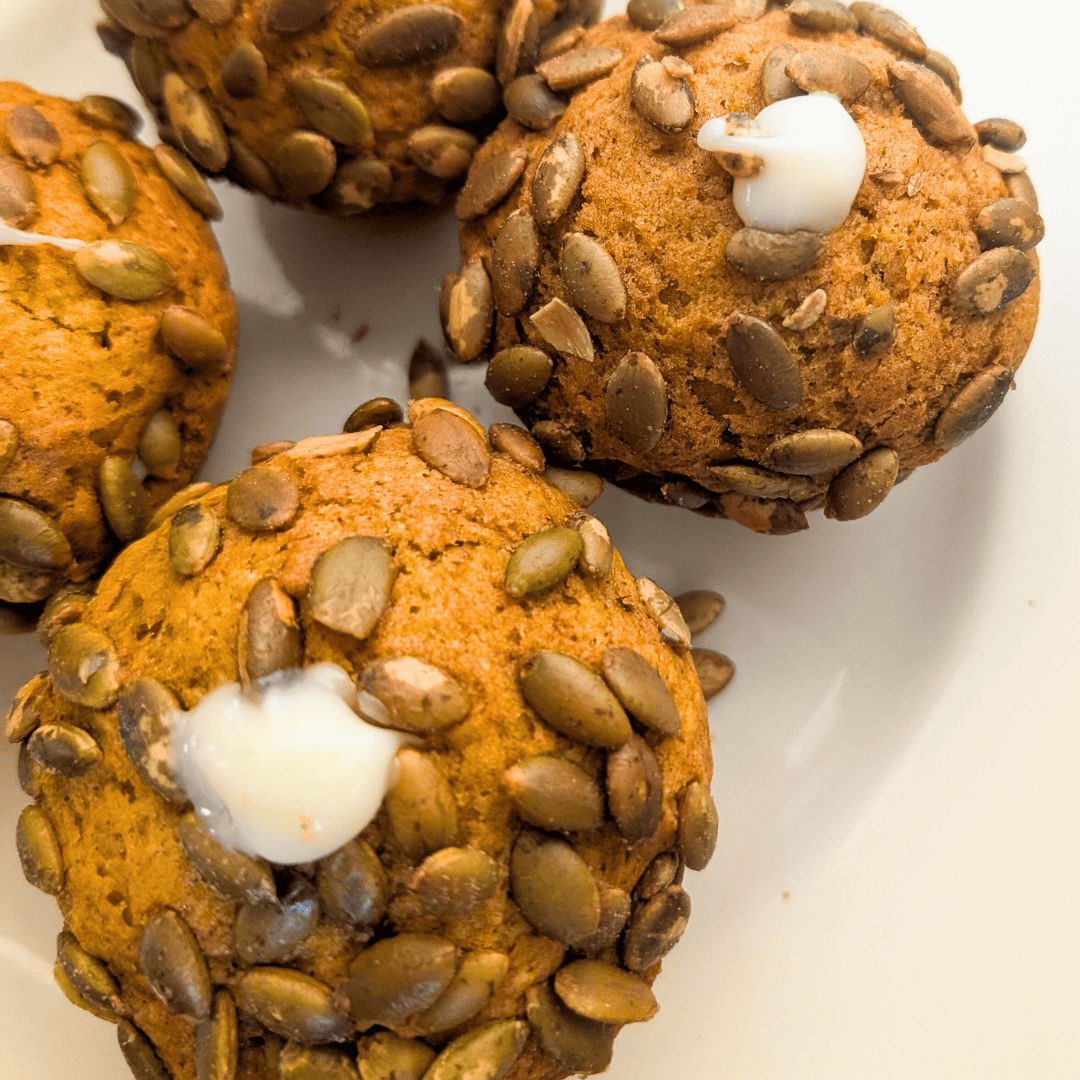 Pumpkin muffins with pumpkin seeds and white icing topping| Freshly baked pumpkin muffins topped with crunchy pumpkin seeds and a touch of icing. Perfect for fall baking.| Delicious homemade pumpkin muffins garnished with pumpkin seeds, featuring moist texture and seasonal flavor.