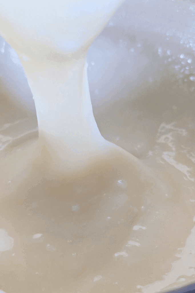 Pouring creamy sauce in a cooking pot, close-up shot.