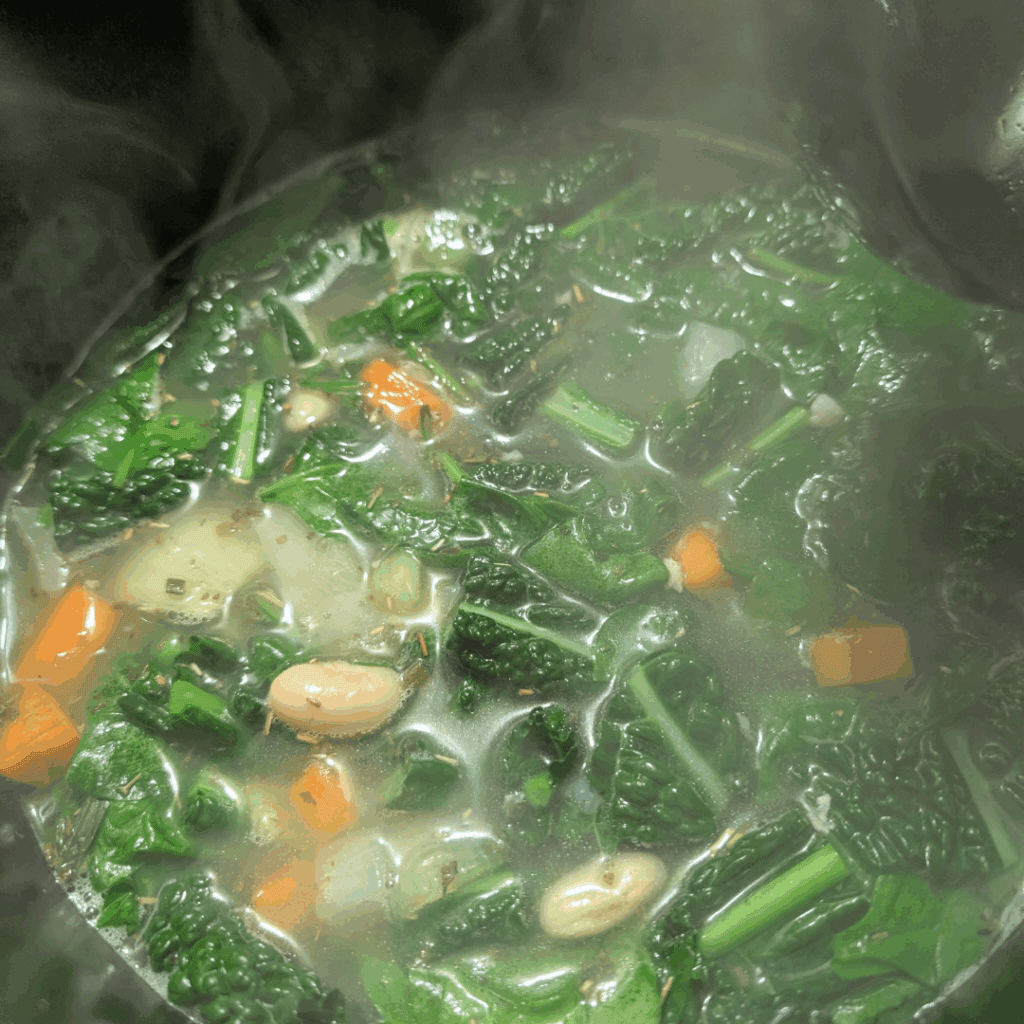 Cooking vegetable soup with greens and vegetables boiling on stove.