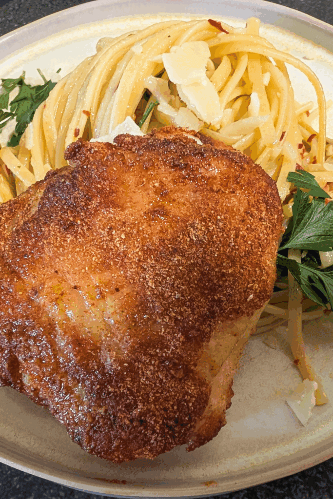 Crispy baked chicken thigh with spaghetti and Parmesan cheese on a plate.