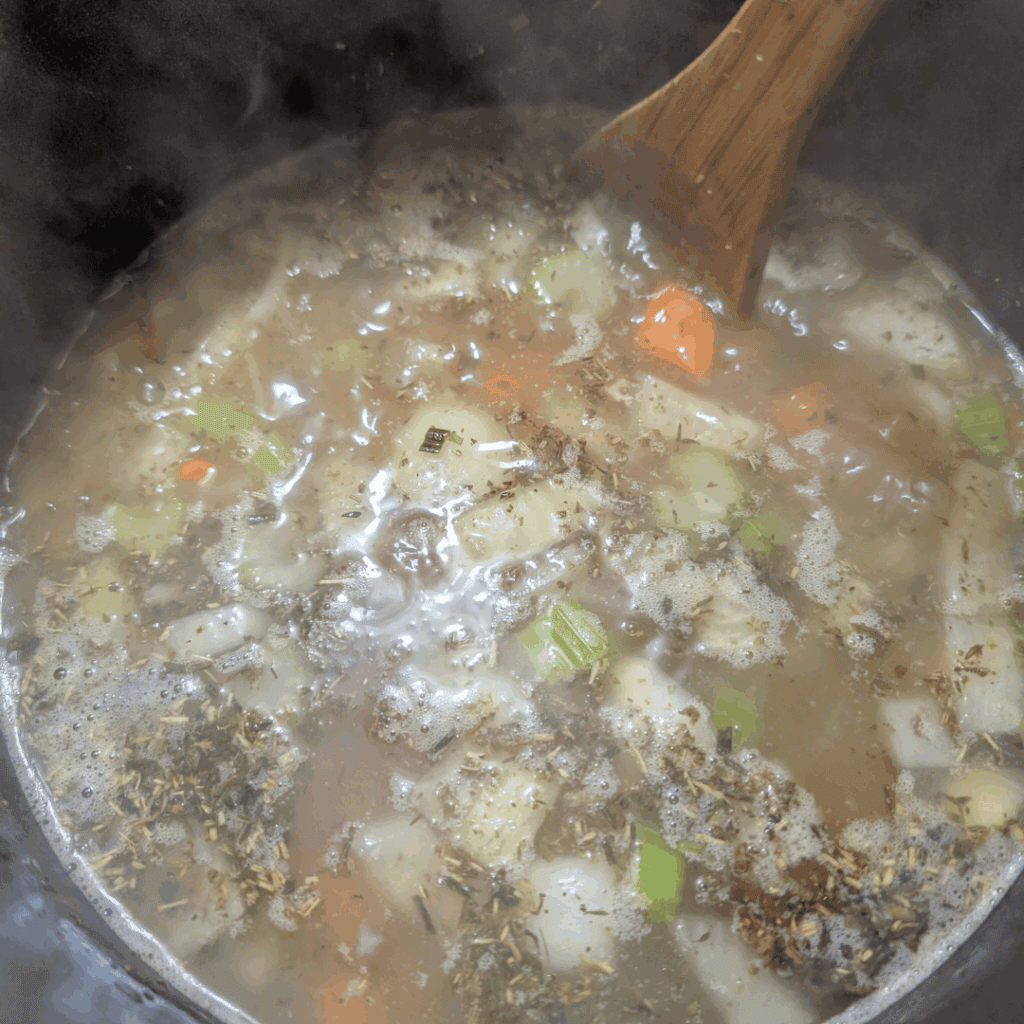Boiling soup with vegetables and herbs in a pot for cooking recipes.