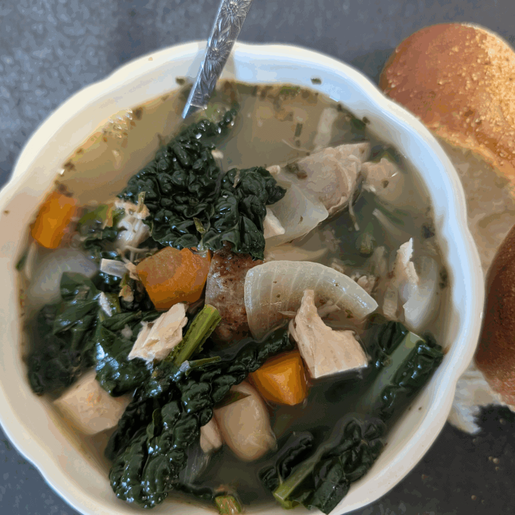 Hearty vegetable and chicken soup with greens and carrots in a white bowl.