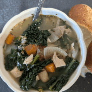 Hearty vegetable and chicken soup with greens and carrots in a white bowl.