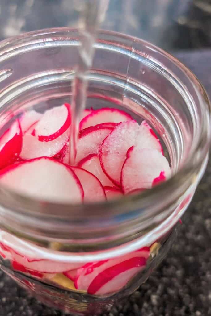 Freshly sliced radishes being pickled in a glass jar for quick preservation.