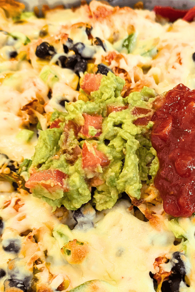 Close-up of creamy guacamole topped with diced tomatoes and salsa on a pizza.