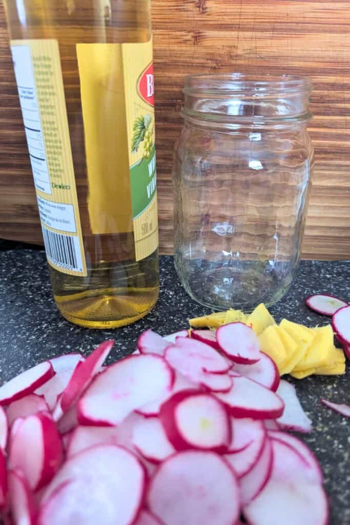 Radishes and vinegar for quick pickling in a mason jar.