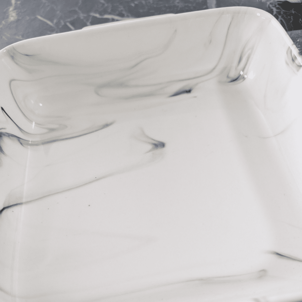 Elegant white marble serving dish for spinach artichoke bake with feta and sun-dried tomatoes.