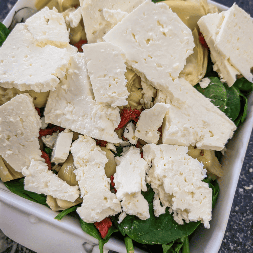 Delicious spinach artichoke bake topped with feta cheese and sun-dried tomatoes, perfect for a healt.