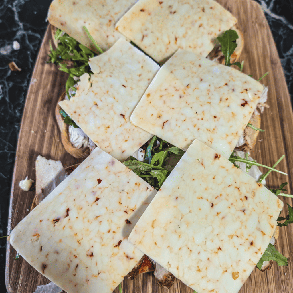 Cheese slices on a wooden board with fresh greens, perfect for cheese lovers and snack enthusiasts.