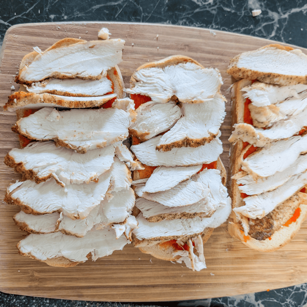 Chicken sandwiches with bread and fillings on a wooden cutting board.