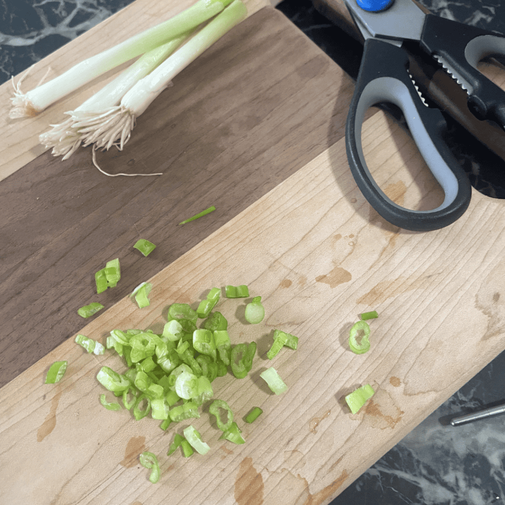 Freshly chopped green onions on a wooden cutting board for cooking.