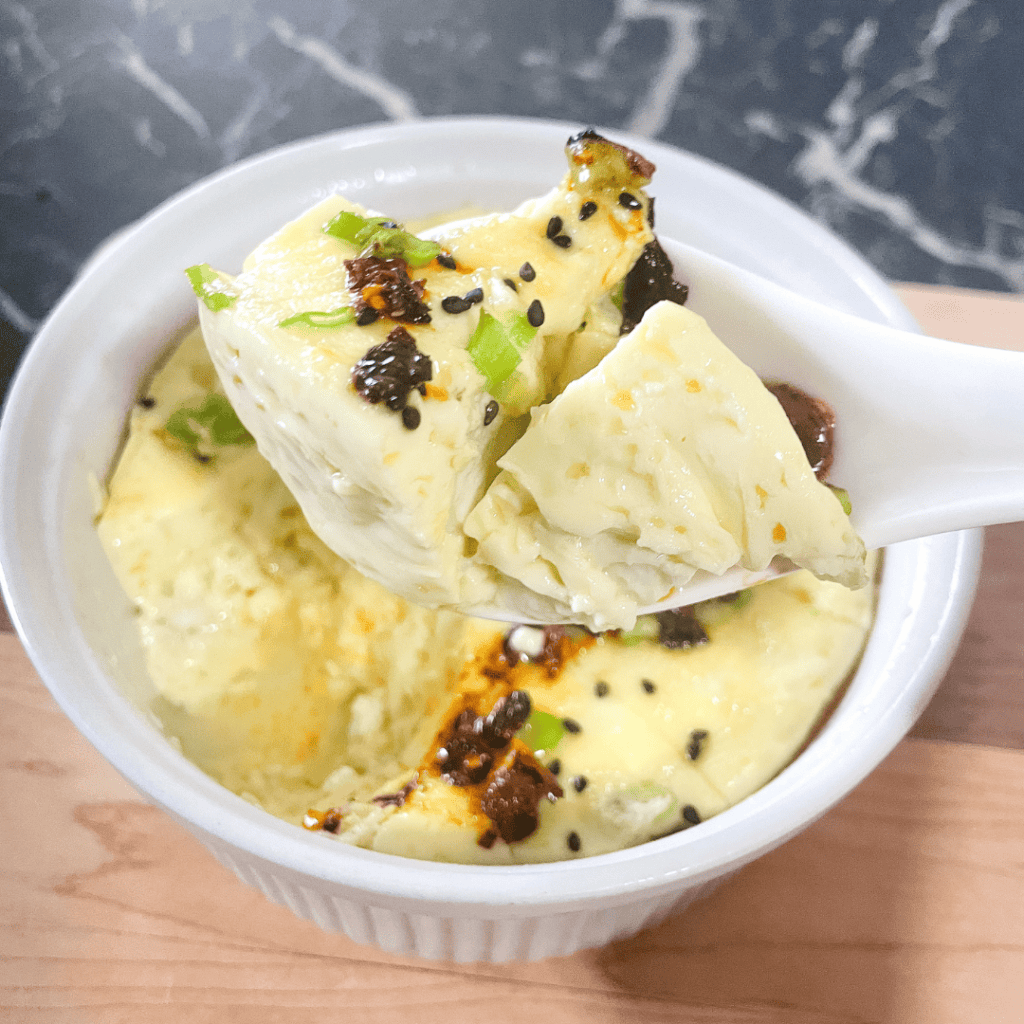 Creamy mashed potatoes topped with black pepper and herbs in a white bowl.