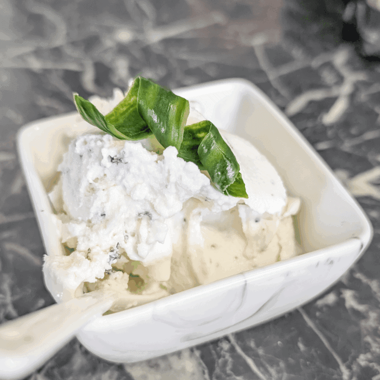 Delicious homemade vanilla ice cream topped with fresh green garnish, served in a white bowl.