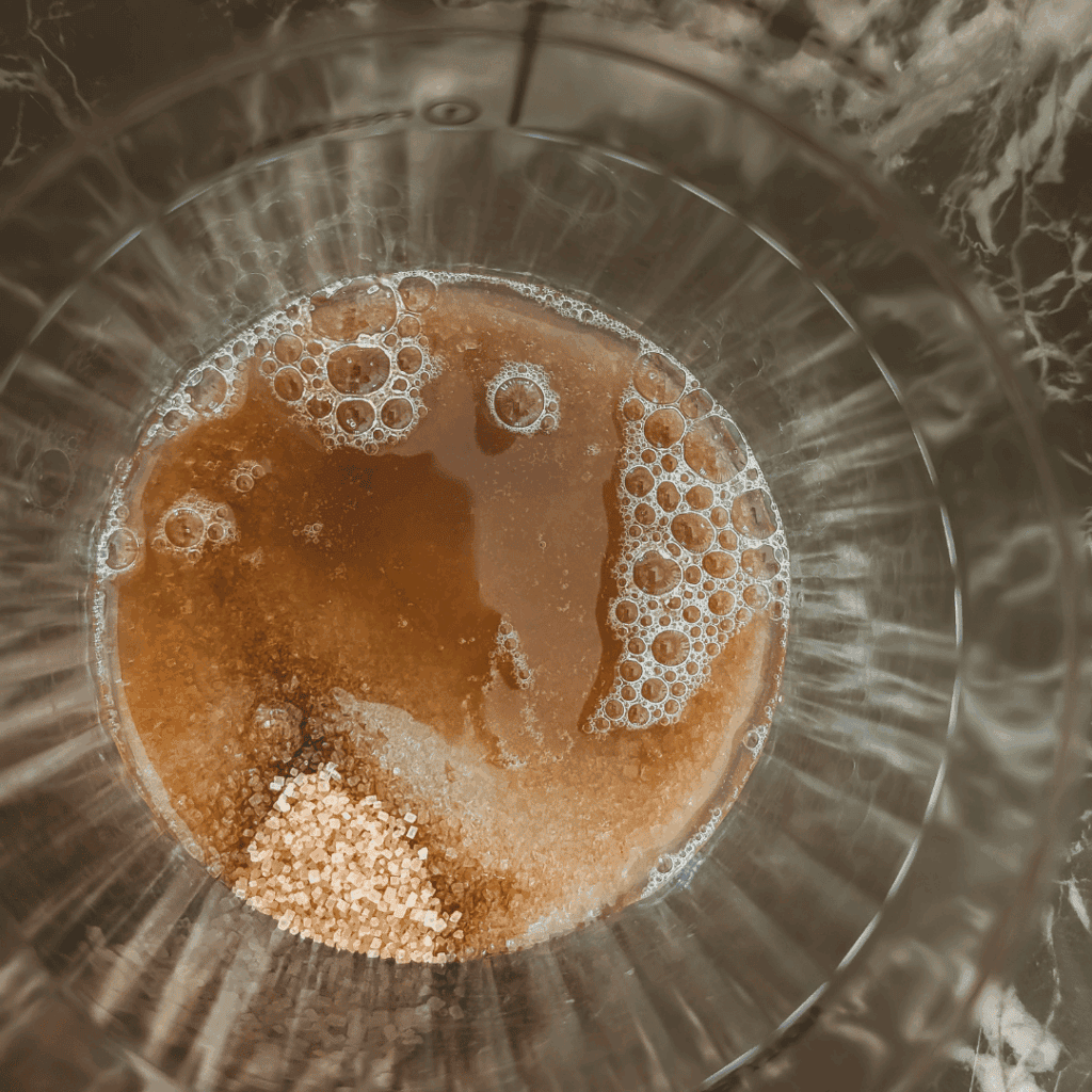 Close-up of homemade caramel sauce in a glass bowl with bubbles and rich color.