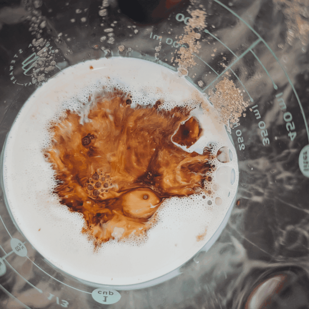 Coffee pouring into a measuring cup with foam and swirling patterns.