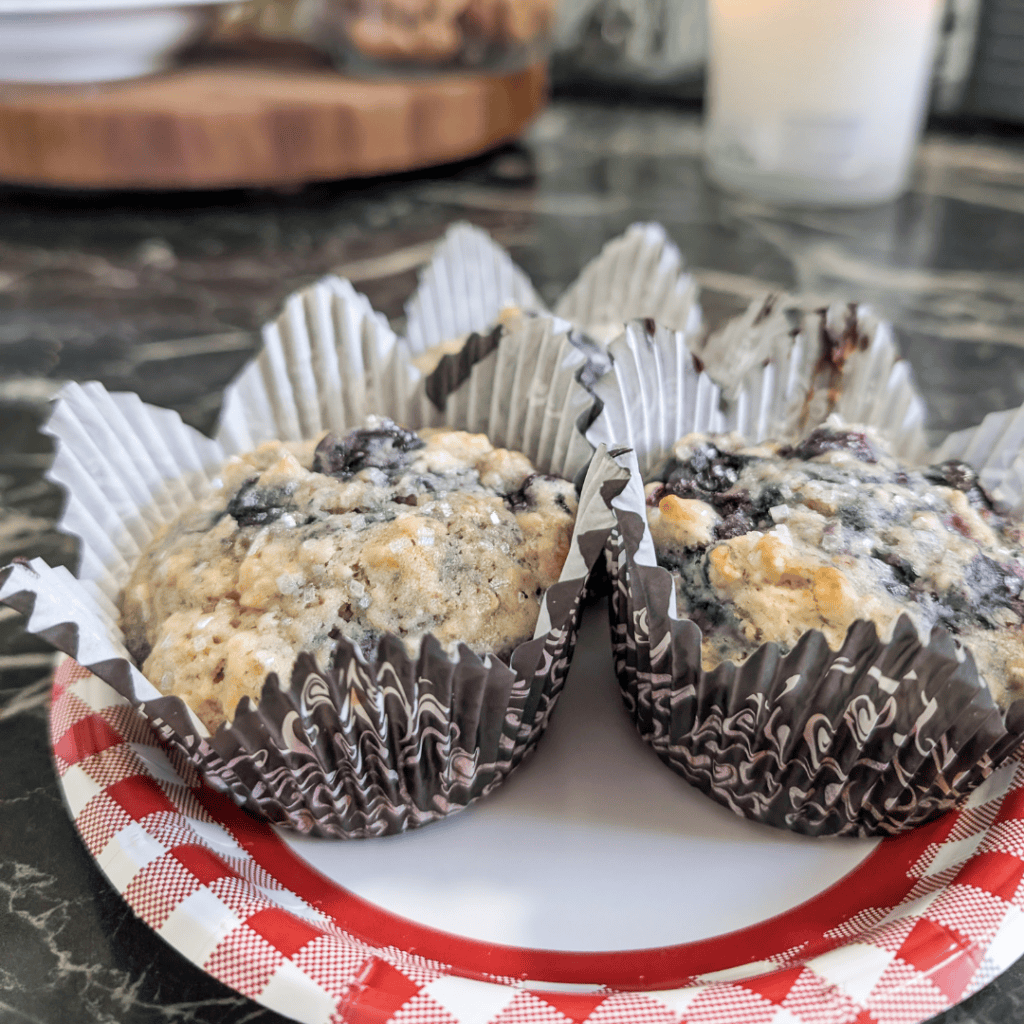 Blueberry muffins in paper liners on a white plate, fresh and baked to perfection.