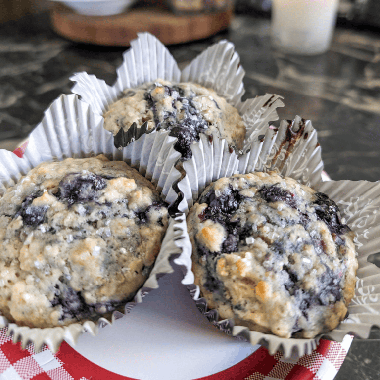 Freshly baked blueberry muffins with crumb topping in paper liners on a plate.