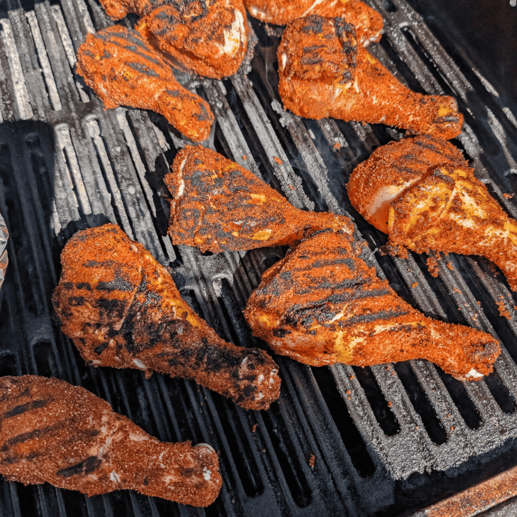 Juicy grilled chicken drumsticks with smoky spice rub on grill.