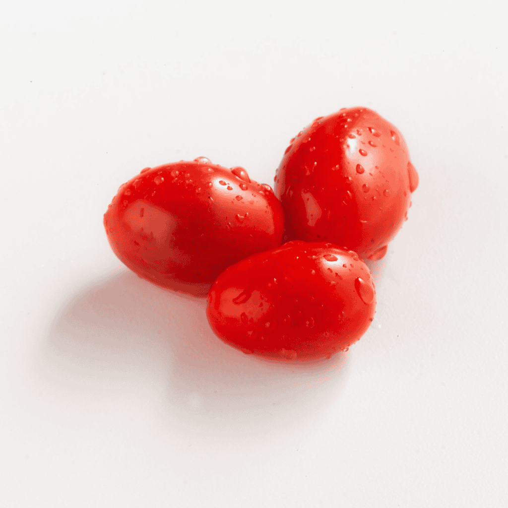 Three fresh cherry tomatoes with water droplets on a white background.