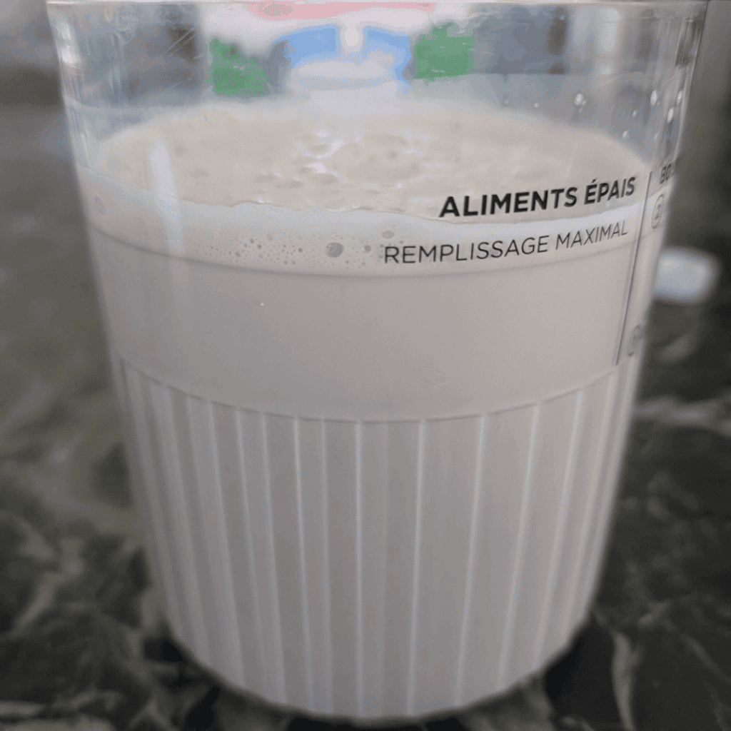 Milkshake in a measuring cup with "ALIMENTS ÉPAIS" label, on a dark marble surface.