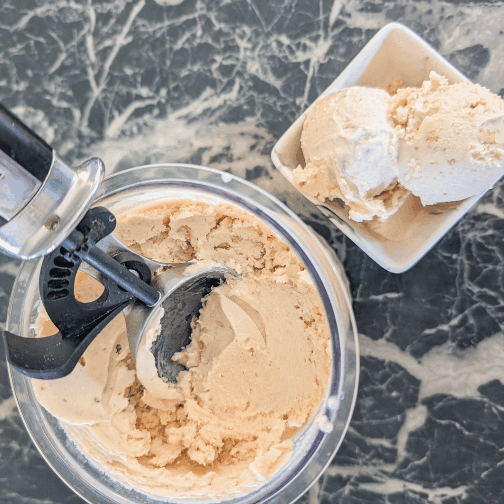 Freshly made vanilla ice cream in an ice cream maker on a marble countertop.