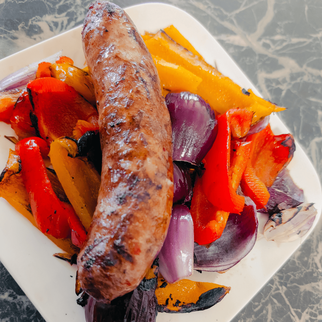 Juicy grilled sausage served with colorful roasted peppers and onions on a white plate.