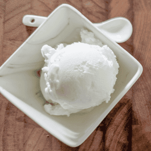 Creamy vanilla ice cream scoop in a white bowl on wooden surface.
