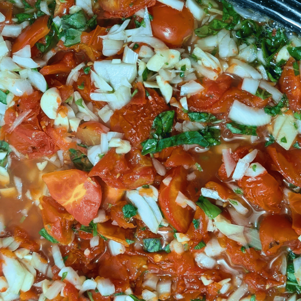 Close-up of homemade roasted tomato sauce with chopped onions and herbs.