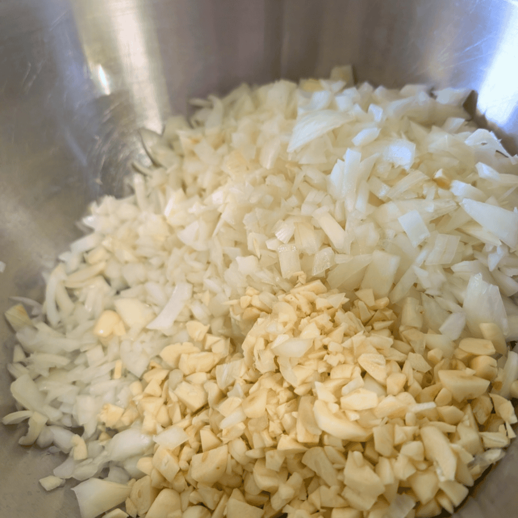Chopped onions and garlic in a metal bowl for homemade tomato sauce.