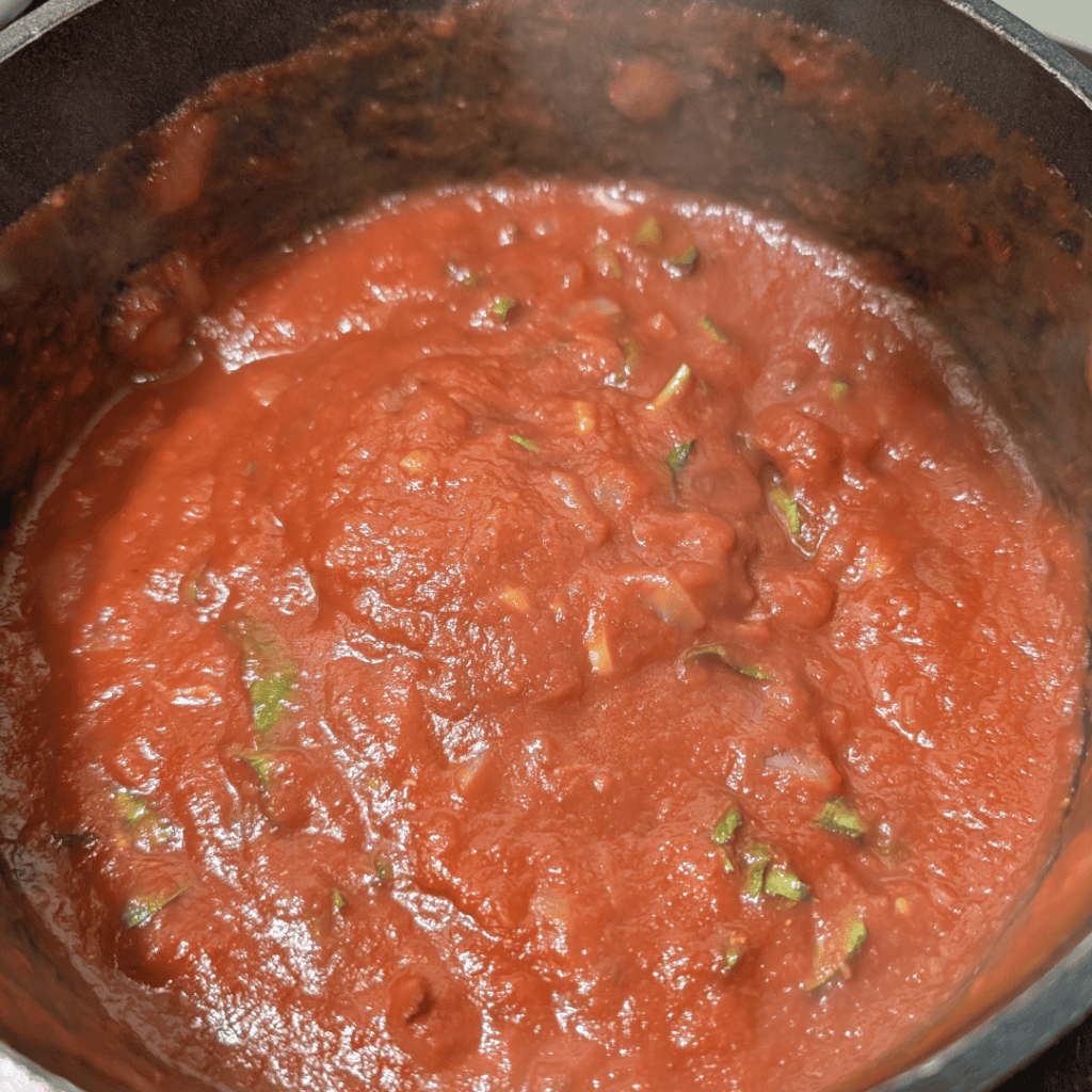 Close-up of simmering homemade tomato sauce with herbs in a pan.