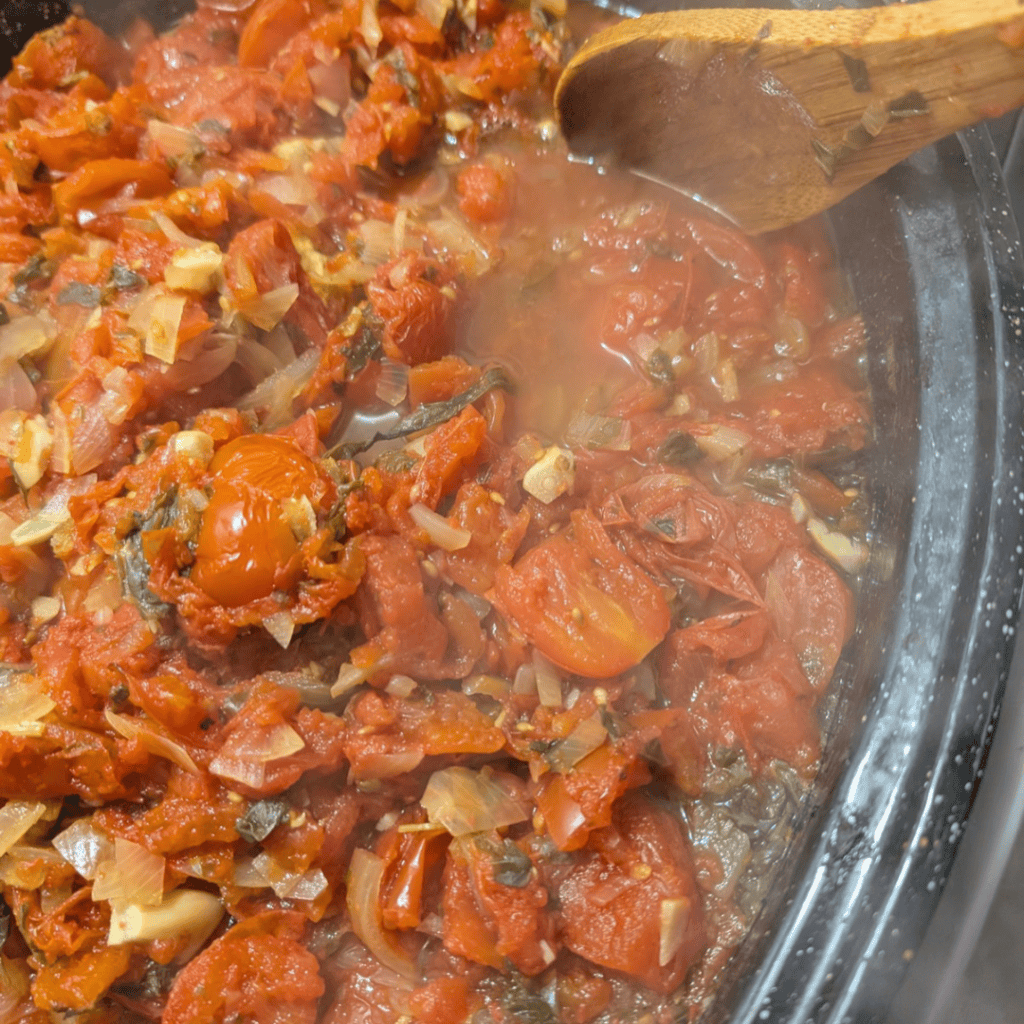 Freshly cooked roasted tomato sauce in a pan with a wooden spoon.
