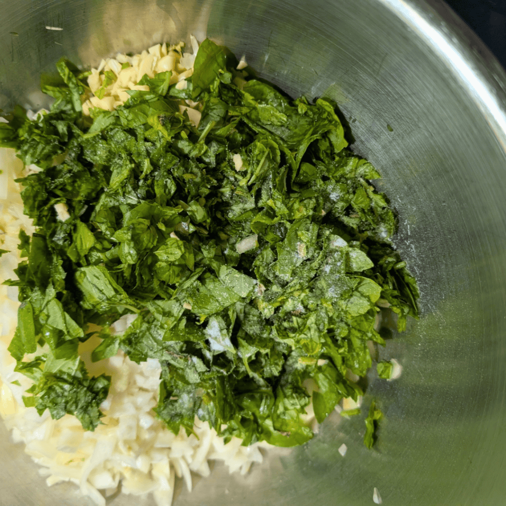 Chopped herbs and garlic in a mixing bowl for homemade tomato sauce.
