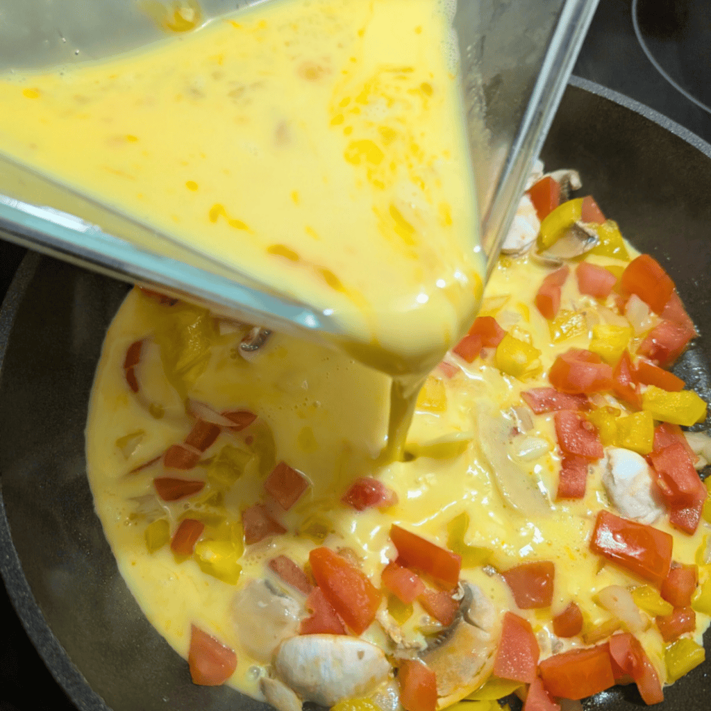 Pouring eggs into a skillet with vegetables for a farm-style omelet.