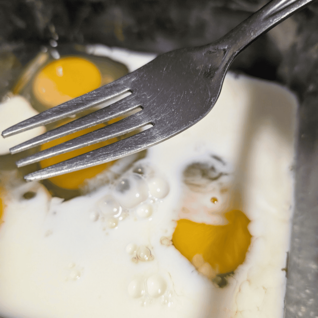 a fork above the eggs and milk in glass dish