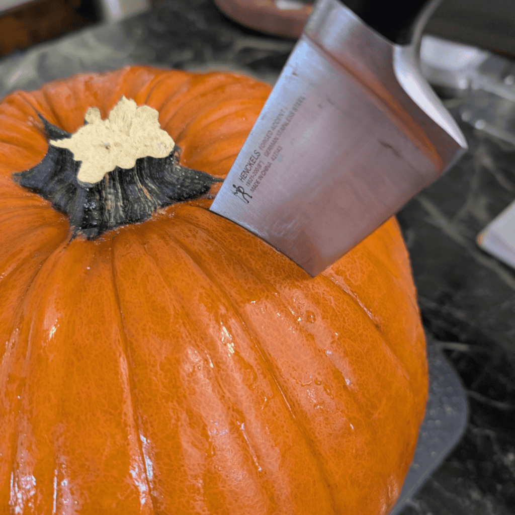 showing butcher knife sticking into the top of whole pumpkin by stem