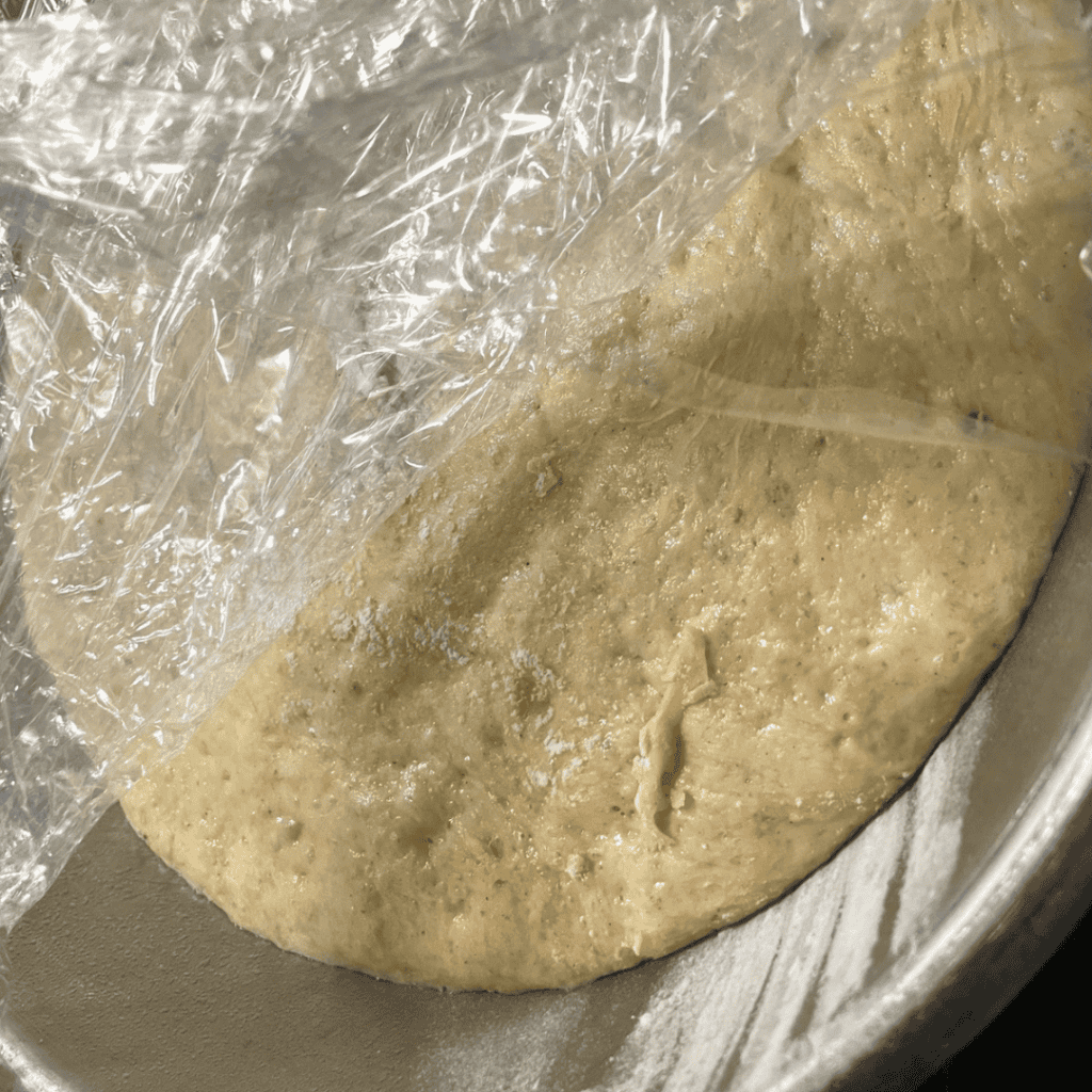 Banana bread cinnamon roll dough in a mixing bowl with plastic wrap.