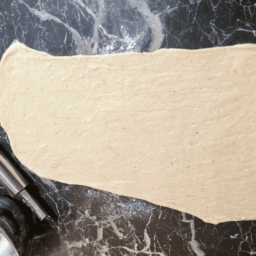 Raw dough for banana bread cinnamon rolls with chocolate chips on a black marble surface.