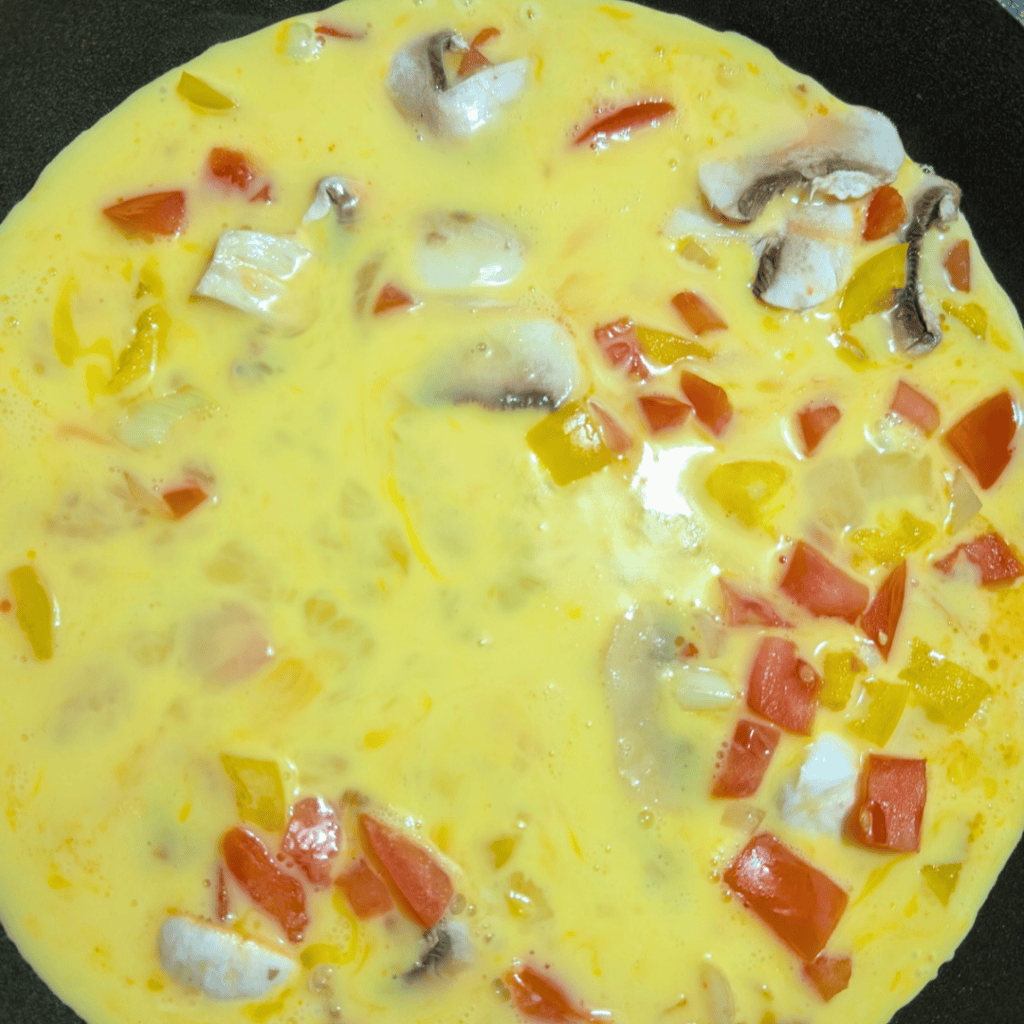 Vegetable omelet with mushrooms, tomatoes, and peppers in a skillet.