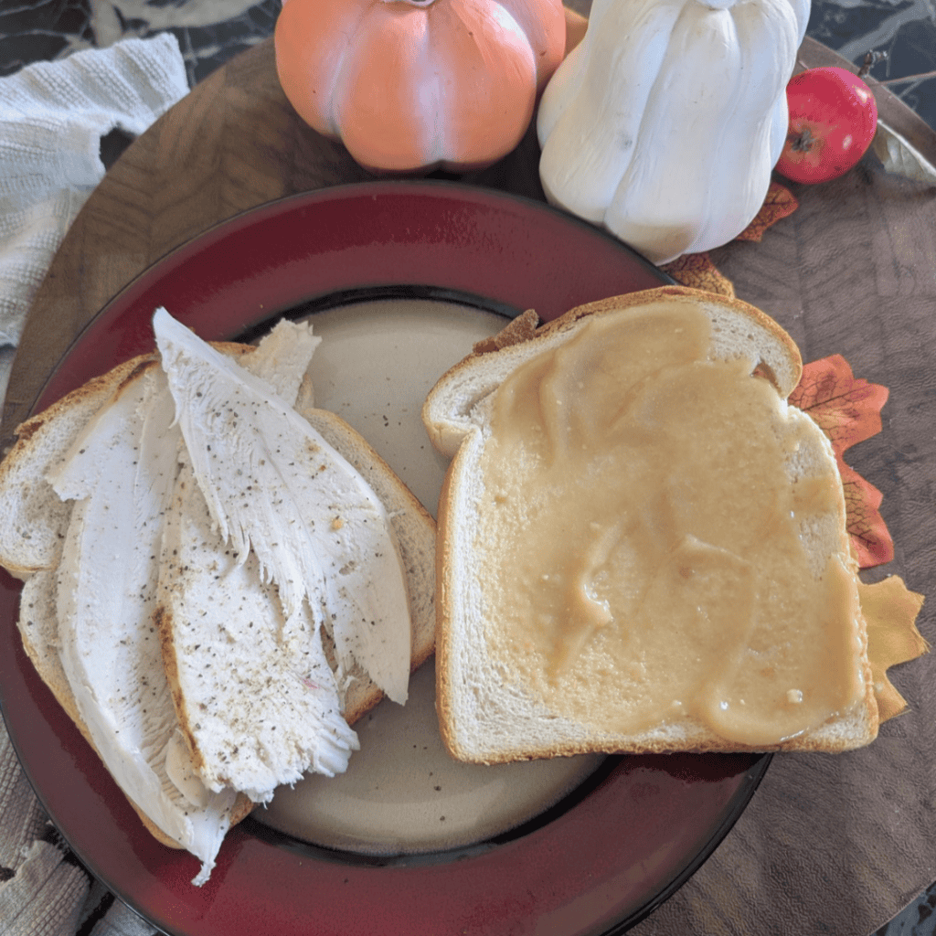 old fashioned mayonnaise on one side of white bread and the other has slices of turkey breast sitting on red rimmed plate in fall tablescape