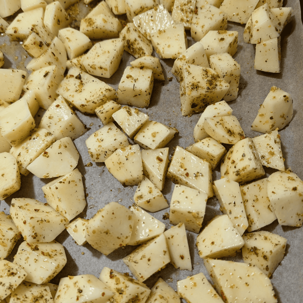 adding spice to cubed potatoes and spreading on baking sheet