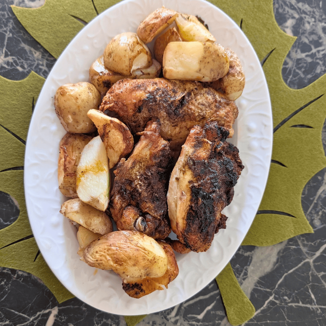 roasted chicken and potatoes on white plate with green maple leaf placemat underneath