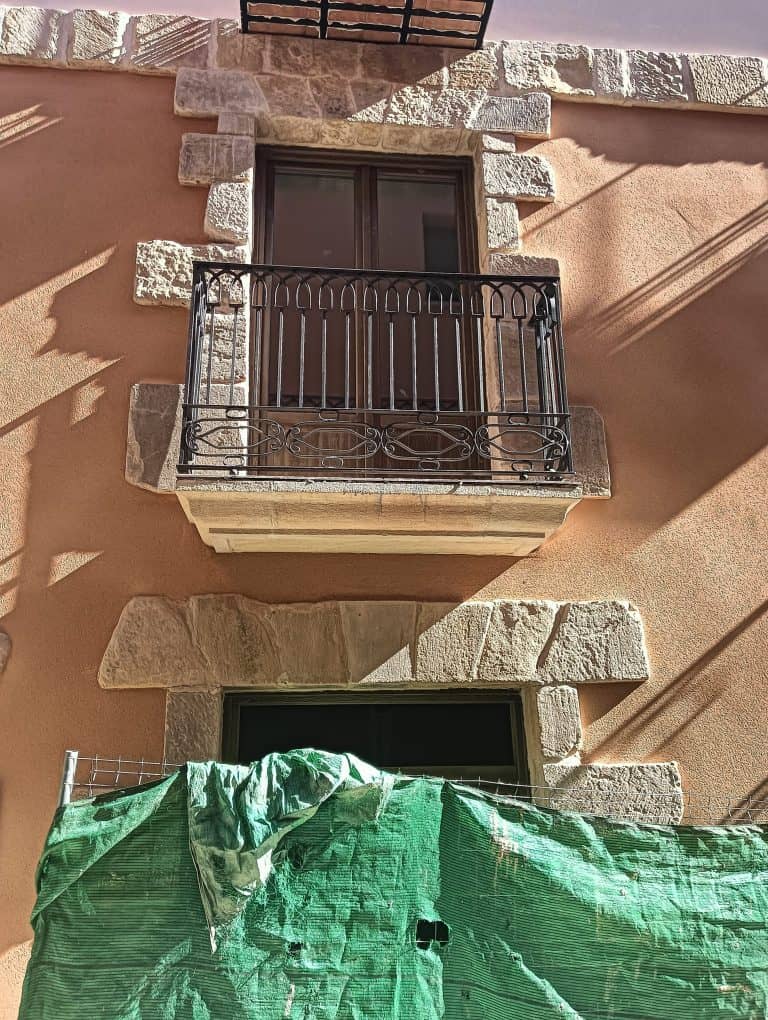 Puerta balcón con barandilla de hierro y marco de piedra en fachada exterior en reparación.