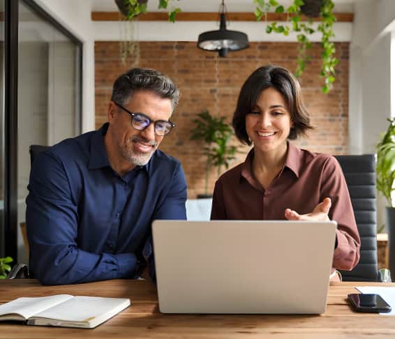 Colleagues at a modern office desk with laptop, notebook, and smartphone for cloud infrastructure management.