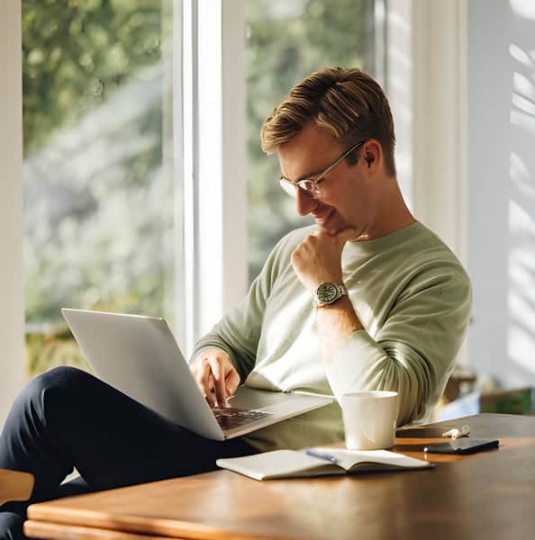 Remote worker with laptop, notebook, pen, and coffee by a window for cloud computing workspace solutions.