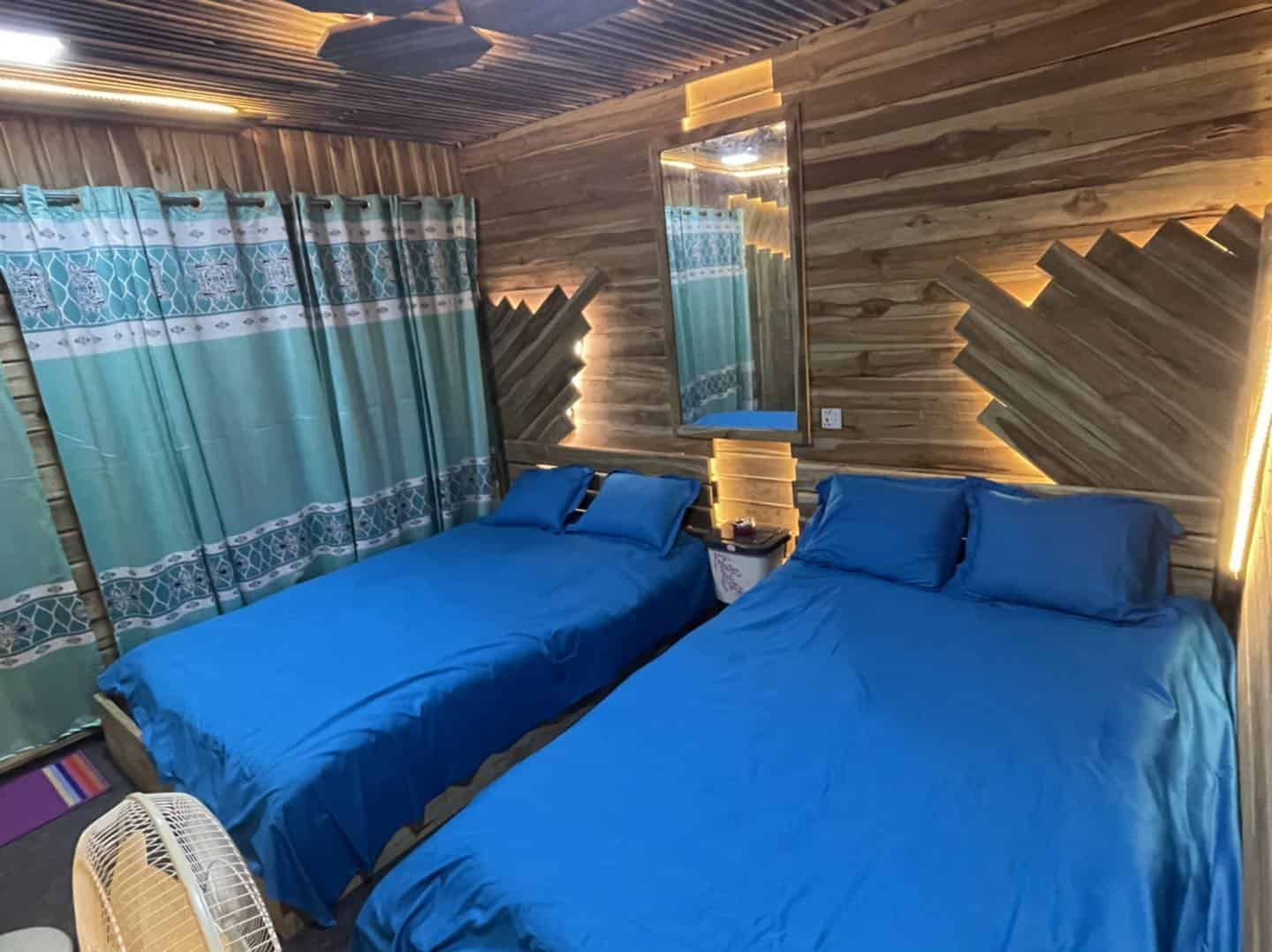Cozy bedroom with blue bedding, wooden walls, and ambient LED lighting for a relaxing stay.