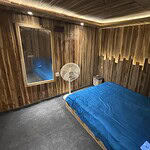 Cozy wooden bedroom with blue bedding, modern lighting, and a fan for comfort.