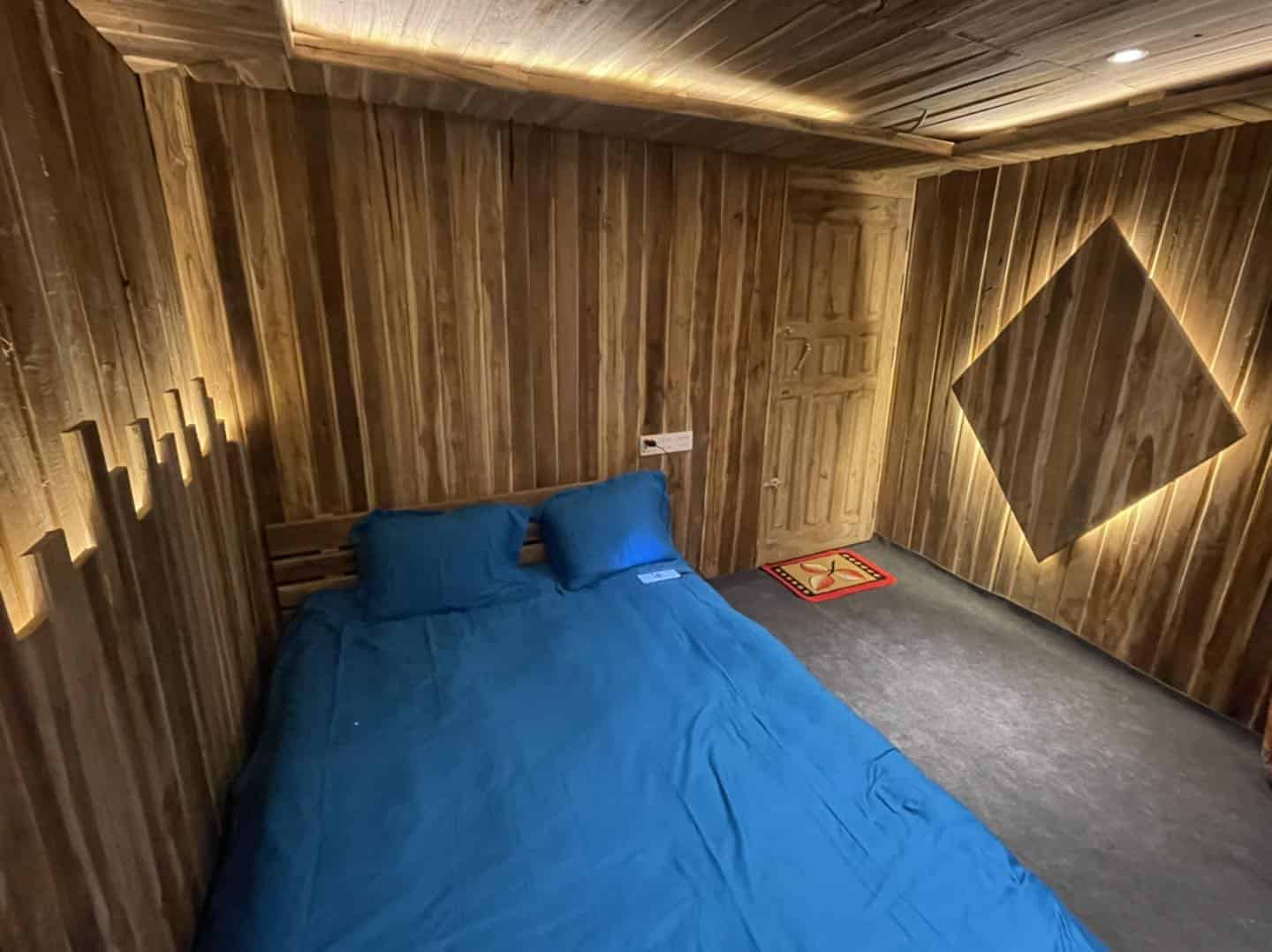 Cozy wooden cabin bedroom with blue bedding and ambient lighting, perfect for a relaxing stay.