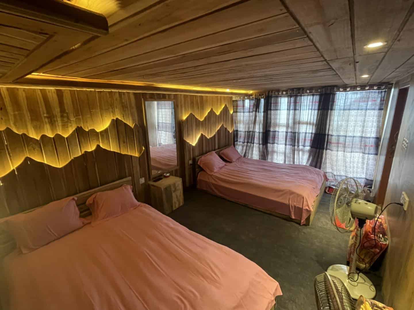 Cozy wooden cabin bedroom with two pink beds, warm lighting, and modern decor for a relaxing stay.